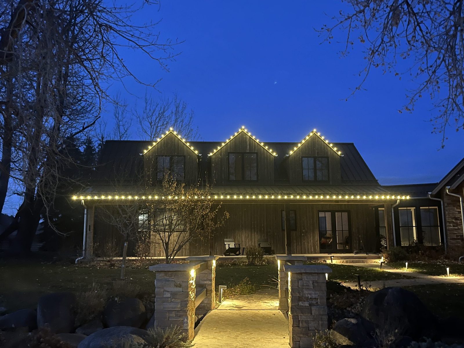 Christmas lights outlining the gables and porch roofline of a farmhouse near Boulder, CO, at dusk