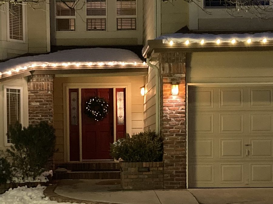 Lit wreath on a red front door, with roofline lights above